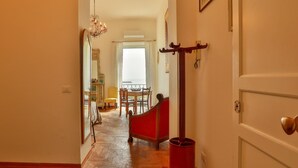 A hallway with a red chair, a wooden table, and a chandelier.