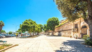 A paved street lined with trees and parked cars, leading to a historic building with an arched entrance.