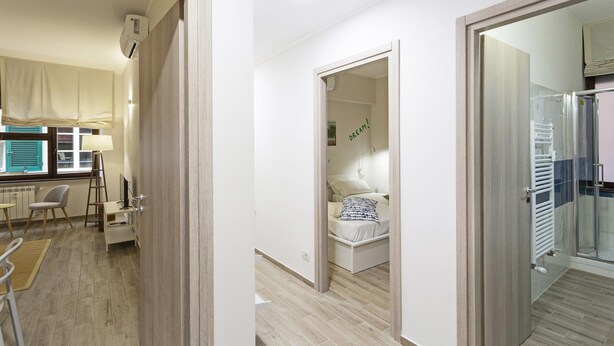 A modern hotel room with a wooden floor, a desk with a chair, a bed with a pillow, and a glass shower area. - XXV Aprile - Basilico by Wonderful Italy (Genoa)