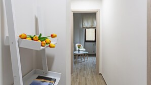 A narrow hallway with a white wall, a small table with a vase of yellow flowers, and a chair. - XXV Aprile - Basilico by Wonderful Italy (Genoa)
