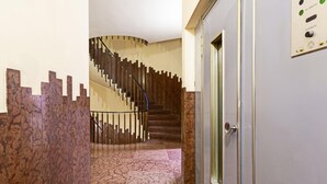 A hallway with a marble floor, a wooden wall panel, and a spiral staircase. - XXV Aprile - Basilico by Wonderful Italy (Genoa)