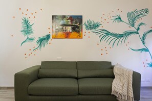 A green sofa in a room with a wall-mounted painting and decorative leaf decals.