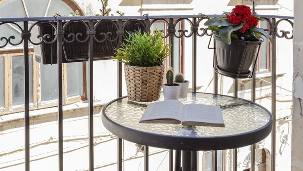 A balcony with a round glass table, two hanging planters with plants, and a view of buildings in the background. - Salomone Apt 8 With Balcony by Wonderful Italy (Syracuse)
