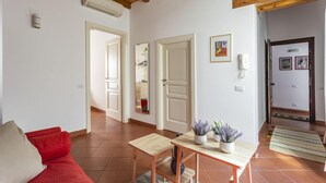 A living room with a red sofa, a wooden coffee table, and a small table with plants. There are two doors leading to other rooms, and a phone on the wall. - Salomone Apt 8 With Balcony by Wonderful Italy (Syracuse)