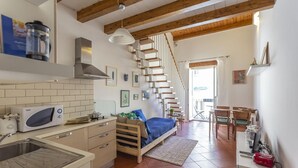 A compact kitchen with a microwave, stove, and sink. A wooden staircase leads to a dining area with a table and chairs. - Salomone Apt 8 With Balcony by Wonderful Italy (Syracuse)