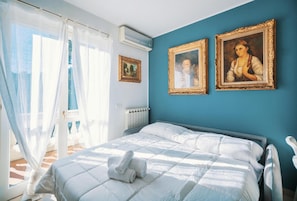 Ein Schlafzimmer mit einem Bett, einem Fenster mit durchsichtigen Vorhängen und zwei gerahmten Bildern an der Wand.