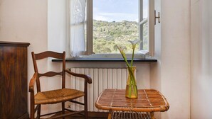 A room with a wooden chair, a wicker table, and a view of a hilly landscape through a window. - Villa Rica by Wonderful Italy (Santa Margherita Ligure)