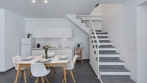 A modern kitchen with white cabinets, a dining area with a wooden table and white chairs, and a staircase with a white railing.