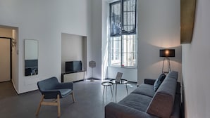 A modern living room with a sofa, a chair, a TV, a small table, and a window with curtains.