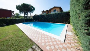 Ein rechteckiger Pool mit gefliestem Rand, umgeben von einem gepflegten Rasen und einer Hecke.