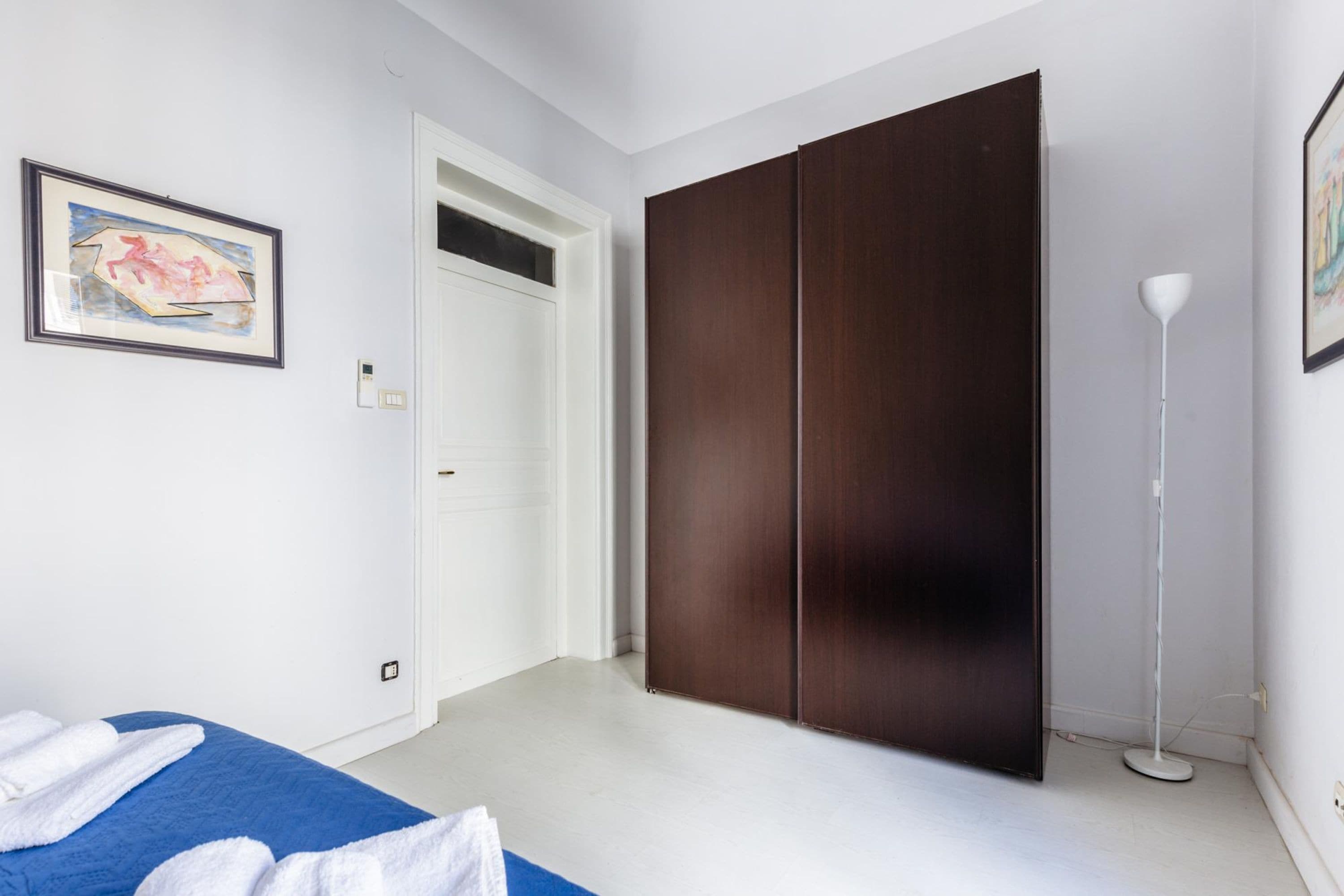 Un dormitorio con cama, armario y lámpara de pie.