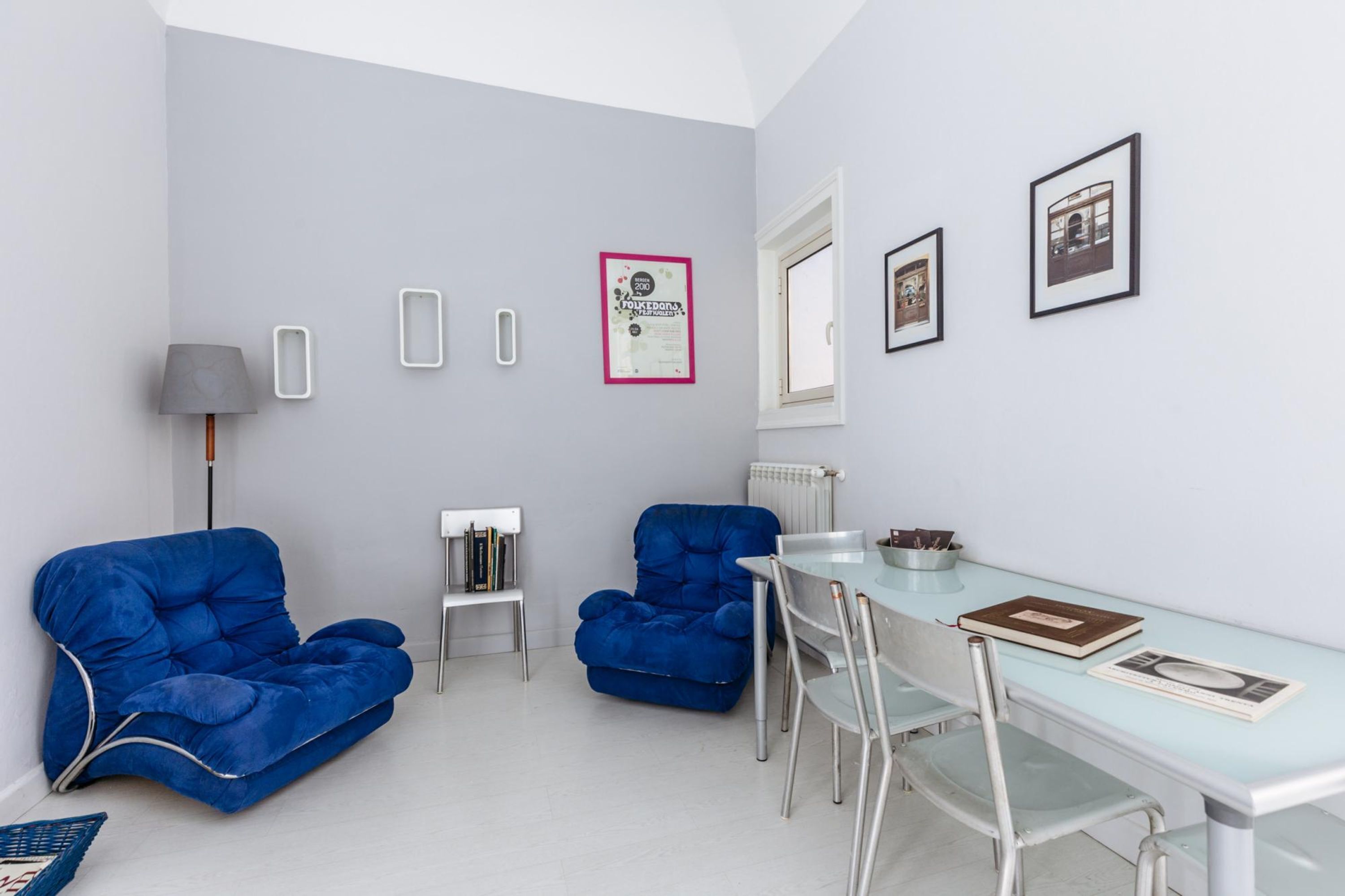 Un soggiorno moderno con un tavolo da pranzo in vetro, due poltrone blu, una lampada e quadri appesi al muro.