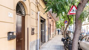 Eine schmale Stadtstraße mit abgestellten Motorrädern und Autos, einem Fußgänger und einem Verbotsschild für das Parken.