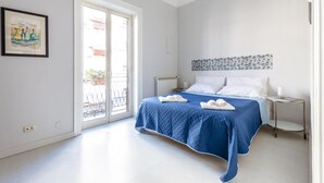 Ein Schlafzimmer mit Bett, Nachttisch, Heizkörper, Fenster und Tür.