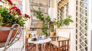 A small outdoor balcony with a table, chairs, potted plants, and a window with a metal grid. - Un Giardino Segreto a Palermo by Wonderful Italy (Palermo)