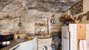 A rustic kitchen with stone walls, a wooden cabinet, and various kitchen utensils. - Casa Petra by Wonderful Italy (Modica)