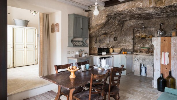 A rustic kitchen with stone walls, wooden cabinets, and a dining area with a wooden table and chairs. - Casa Petra by Wonderful Italy (Modica)