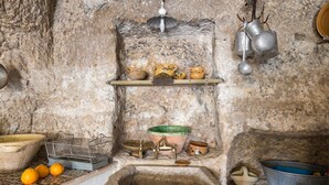 A rustic kitchen with a stone sink, shelves with pottery, and hanging utensils. - Casa Petra by Wonderful Italy (Modica)