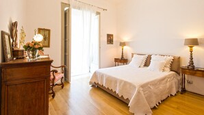 A bedroom with a wooden dresser, a chair, a bed with white bedding, two bedside tables with lamps, and a door leading to another room. - Charming Apartment by Wonderful Italy (Palermo)