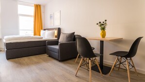 A modern hotel room with a bed, sofa, two chairs, a small table, and a vase with flowers. - Boxi Studios Berlin S (Berlin)