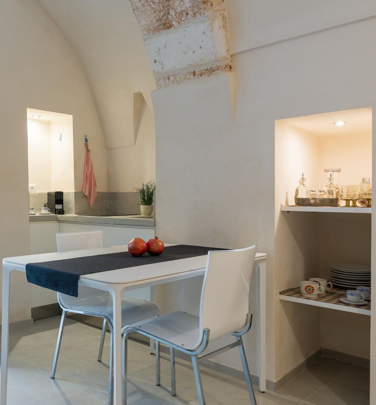 A modern kitchen with white cabinetry, a dining table with two chairs, and a potted plant on the counter.