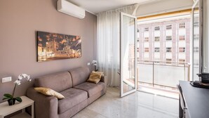 Una sala de estar moderna con un sofá, un cuadro, una planta en maceta y vistas de un edificio a través de un ventanal.