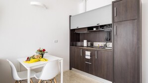 Cocina compacta con armarios de madera oscura, encimera blanca y un pequeño comedor con sillas blancas.