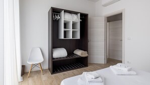 Un dormitorio moderno con un armario amplio, una cama con toallas ordenadas y una silla blanca.