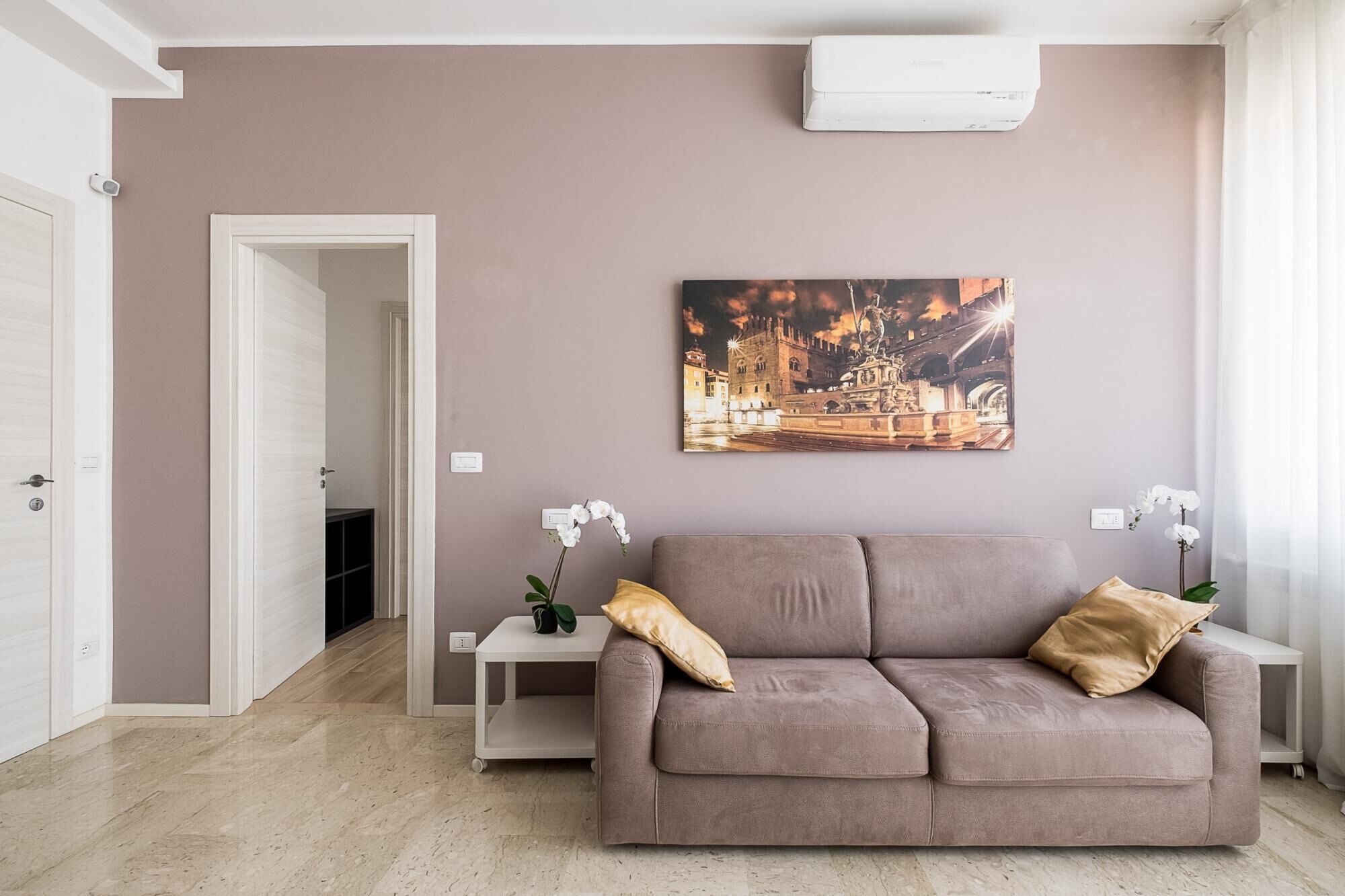 A living room with a beige sofa, a painting of a cityscape, and white orchids on side tables.