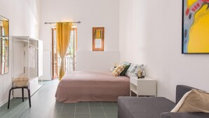 Une chambre à coucher avec un lit, une table de chevet et un canapé. Il y a une fenêtre avec des rideaux, une porte et une petite fenêtre au-dessus du lit.