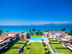 A resort with multiple buildings, a central swimming pool, and a view of the sea.