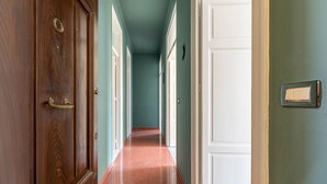 Een gang met houten deuren en witte sierlijsten, die leidt naar een kamer met een rood tapijt.