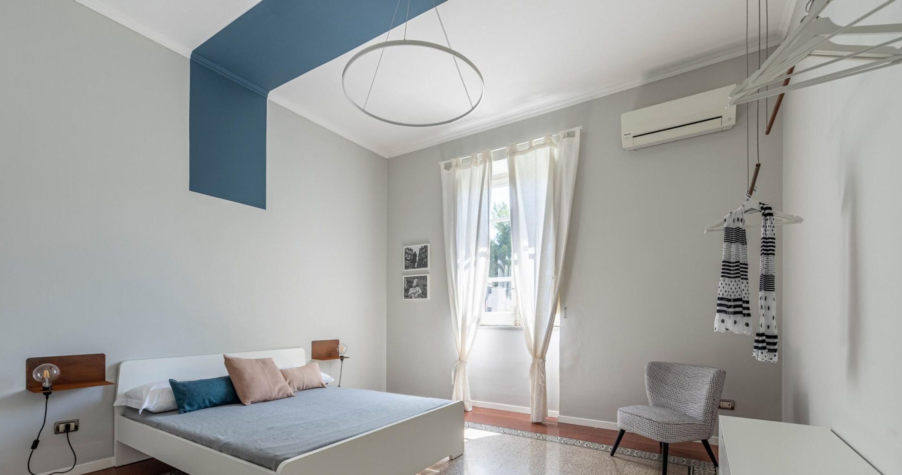 Een moderne slaapkamer met een bed, een stoel, een hanglamp en een raam met gordijnen.