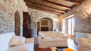 Ein Zimmer mit steinernen Wänden, Holzboden und weißen Sofas, mit einem Tisch und einer Vase darauf.