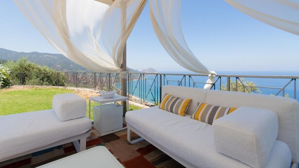 Ein Balkon mit einer weißen Couch und einem kleinen Tisch, mit Blick auf eine malerische Landschaft aus Meer und Bergen.
