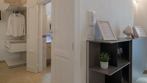 A hotel reception area with a white interior, a reception desk, a phone, a framed menu, a potted plant, and a wine glass. - Isabella Apartment by Wonderful Italy (Ostuni)