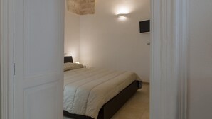 A bedroom with a bed, a nightstand, a wall-mounted TV, and a ceiling light. - Isabella Apartment by Wonderful Italy (Ostuni)