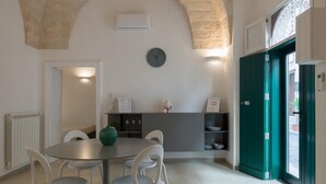 A dining area with a round table, four chairs, a clock on the wall, and a green door. - Isabella Apartment by Wonderful Italy (Ostuni)