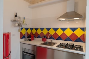Una cucina con un vivace rivestimento a mosaico a forma di rombo, un lavello in acciaio inossidabile, un piano cottura a gas e un frigorifero rosso.