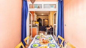 A dining area with a table set for two, a kitchen in the background, and a balcony with blue curtains. - Gaudio Flat Near Ariston Theater by Wonderful Italy (Sanremo)