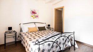 A bedroom with a bed, two bedside tables, a nightstand, a wooden door, and a floral artwork on the wall. - Kalsa Apartment With Terrace by Wonderful Italy (Palermo)