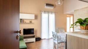 A modern living room with a flat-screen TV, a green sofa, a dining table with chairs, and a large window with curtains. - Kalsa Apartment With Terrace by Wonderful Italy (Palermo)