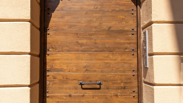 A wooden door with a metal handle and a metal latch, set in an arched doorway with a stone wall. - Kalsa Apartment With Terrace by Wonderful Italy (Palermo)