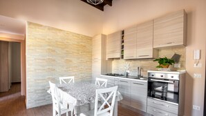 A modern kitchen with a stone backsplash, stainless steel appliances, and a dining area with white chairs. - Kalsa Apartment With Terrace by Wonderful Italy (Palermo)