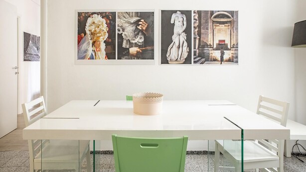 A modern dining area with a white table and chairs, a decorative bowl on the table, and three framed artworks on the wall. - Mirabella Apartment in Ortigia by Wonderful Italy (Syracuse)