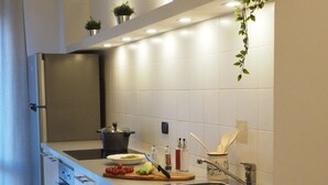 A modern kitchen with white cabinets, a stainless steel refrigerator, a sink, and a countertop with a cutting board and vegetables. - Guglielmo City Center Studio by Wonderful Italy (Bologna)