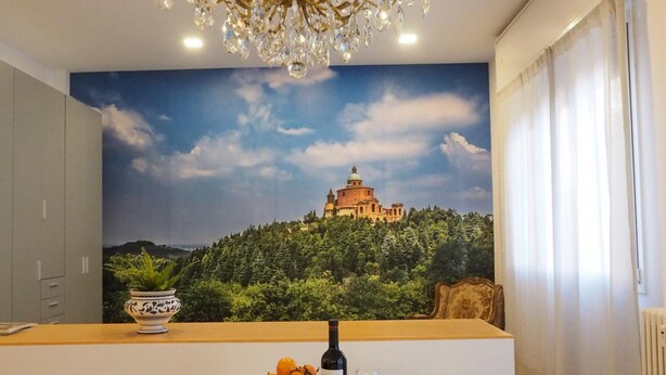 A dining area with a glass table, white chairs, a chandelier, and a mural of a castle on a hill. - Guglielmo City Center Studio by Wonderful Italy (Bologna)