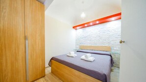 A bedroom with a wooden wardrobe, a bed with a headboard, and a stone wall. - Casa White by Wonderful Italy (Cefalù)