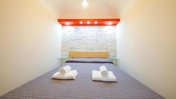 A single bed with a patterned bedspread, a wooden headboard, and two rolled towels on the bed. - Casa White by Wonderful Italy (Cefalù)