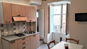 A modern kitchen with wooden cabinets, a gas stove, and a sink. There's a dining table with chairs and a TV mounted on the wall. - Casa White by Wonderful Italy (Cefalù)